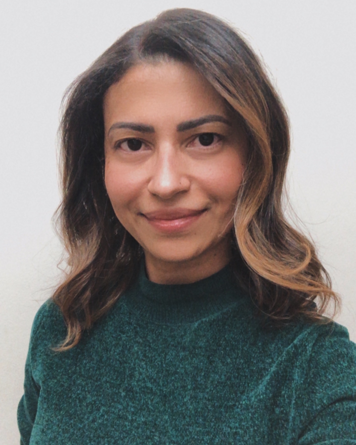 Uma mulher com cabelo solto e escovados, pele negra, com discreto sorriso e vestindo uma blusa verde. Profissional enfermeira esteta